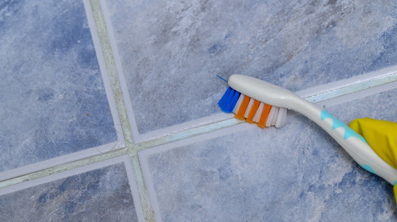 Person cleaning tile grout lines with a toothbrush