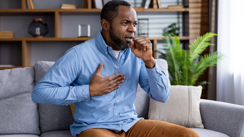 A man holding his chest and coughing