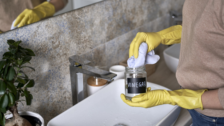 Person wearing gloves, using vinegar as a cleaner in bathroom