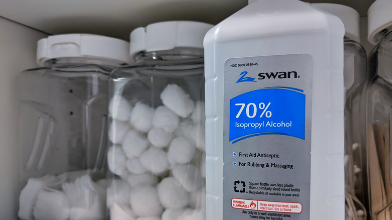 A bottle of isopropyl alcohol on a shelf with a jar of cotton balls and rounds.