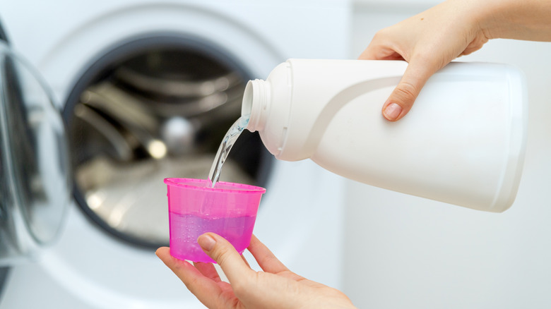 A person pouring laundry detergent into a pink cup.