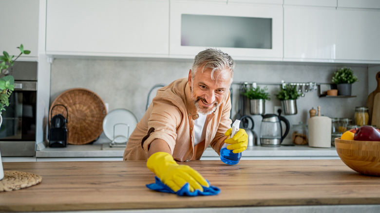 A man cleans off a wooden island with a blue rag and a spray bottle filled with a blue cleaning solution
