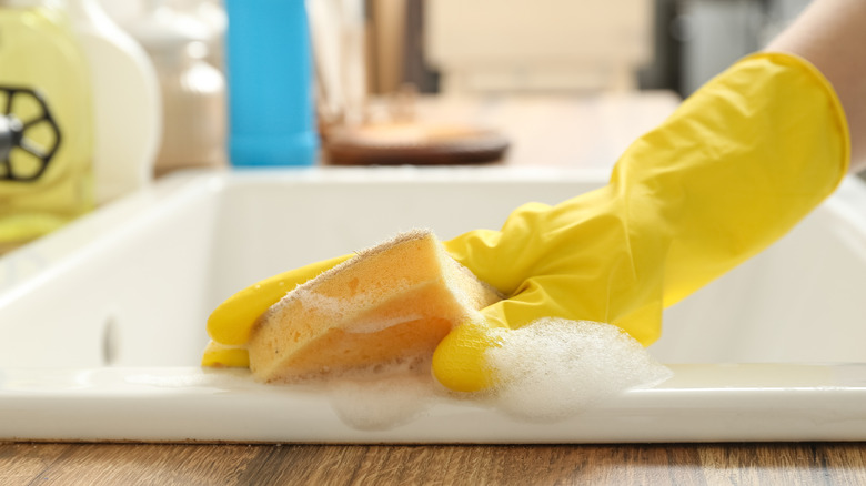 A hand wearing a yellow glove cleaning a sink