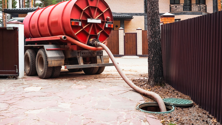 A septic tank pumping truck with a hose leading into an open septic tank