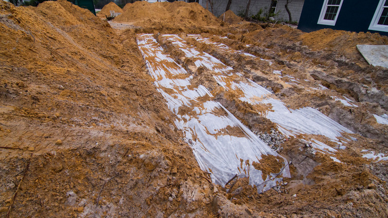 A view of an exposed drainage field in a brown, dirty yard