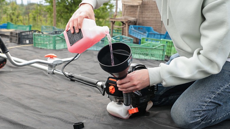 Man pouring a gas/oil mixture into the fuel tank of a weed trimmer