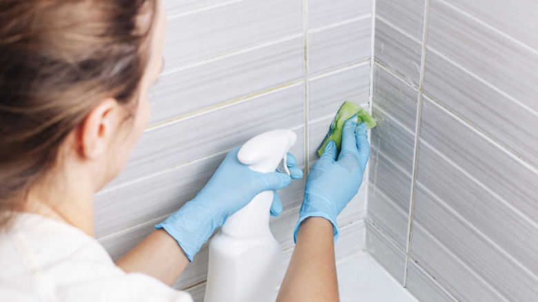 Woman cleaning tiled wall next to bathtub