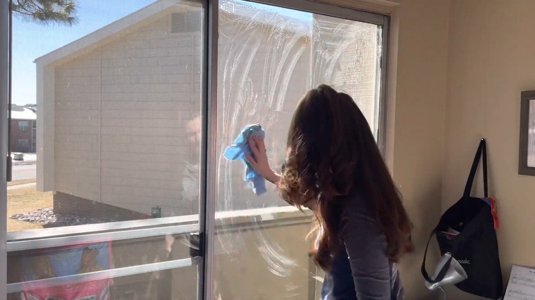 Woman using a microfiber cloth to spread dish soap on a window