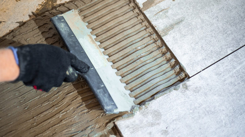 A person applying mortar to the ground for tiles