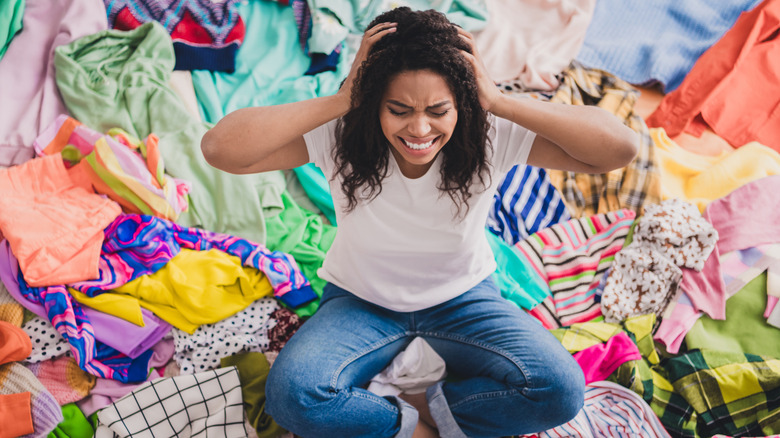 Woman sitting among piles of clothes and feeling overwhelmed