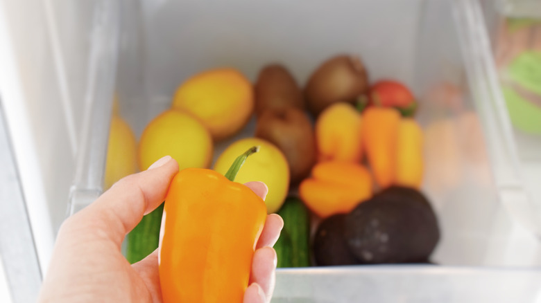 Hand retrieving a bell pepper from a crisper drawer