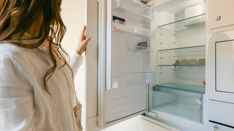 Woman opening an empty fridge with a crisper drawer