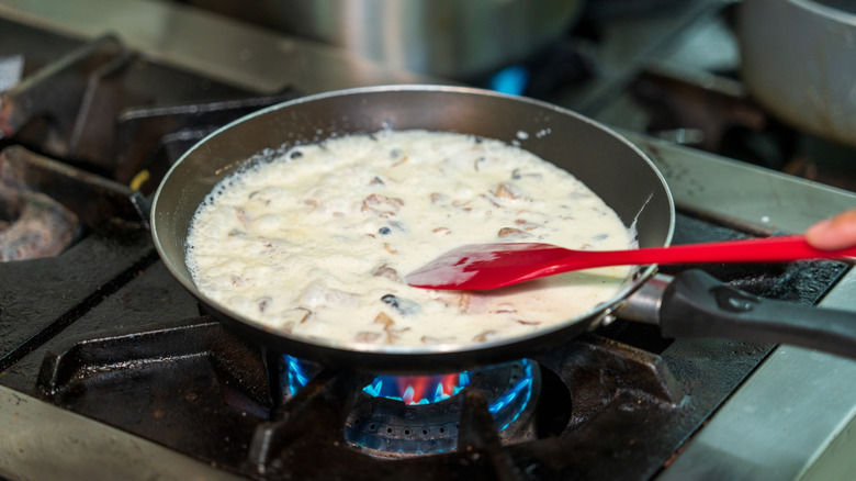 A gas stove with red flames under a pan of creamy sauce