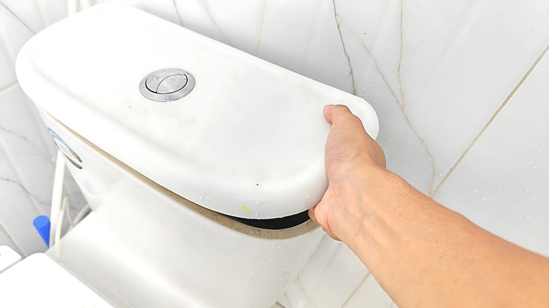 a person lifts a toilet tank lid