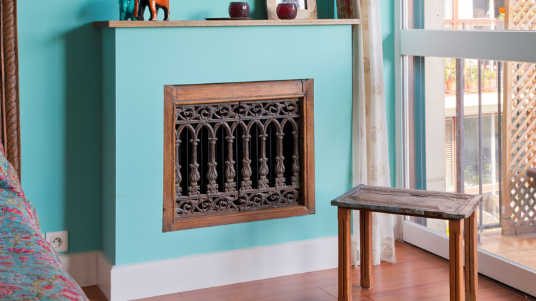 A dark, ornate opening in a light blue radiator cover positioned on a blue wall
