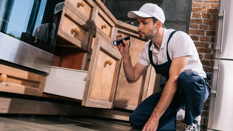 Man inspecting kitchen cabinets and drawers with flashlight