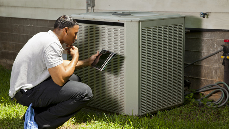 An AC unit with plants and weeds growing around it