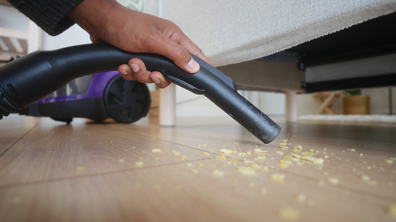 Person holding a vacuum nozzle to suck up crumbs from underneath furniture.