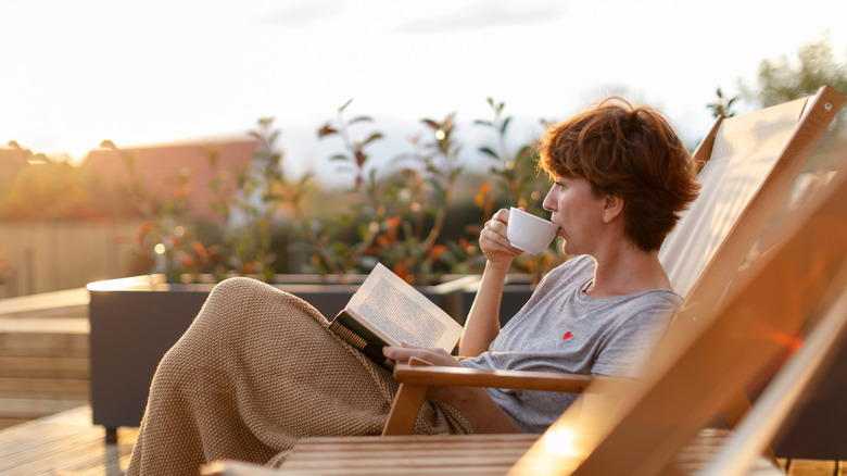 a woman drinks tea and reads a book on a patio