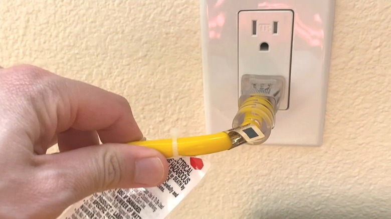 Person plugging a yellow extension cord into the wall