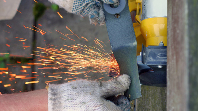 Person sharpening their lawn mower blades with an angle grinder