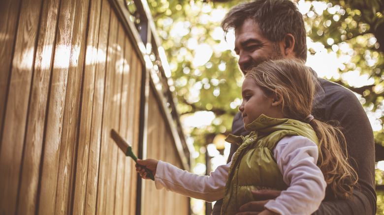 Man staining wood fence with his daughter.