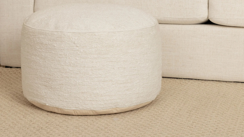 A beige boucle ottoman in front of a matching sofa