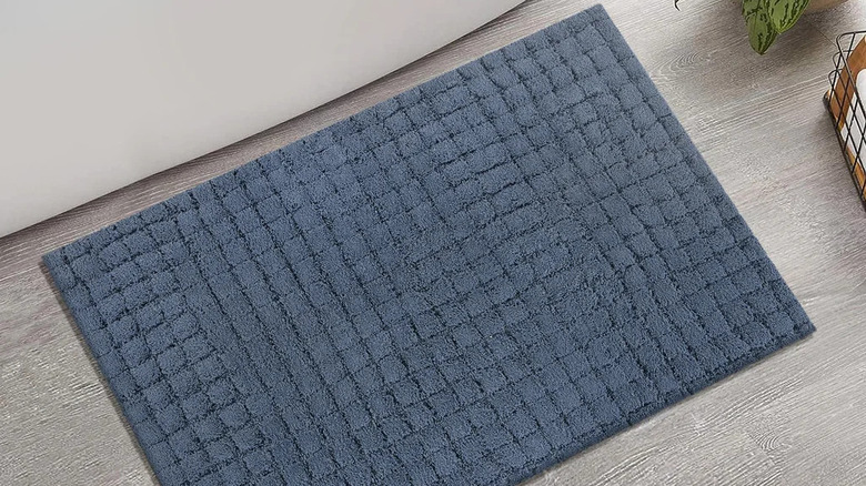 A navy blue bath rug sits on a gray floor