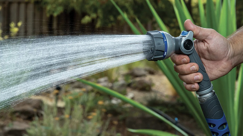 A hand holds a hose outfitted with one of Orbit's nozzles spraying water