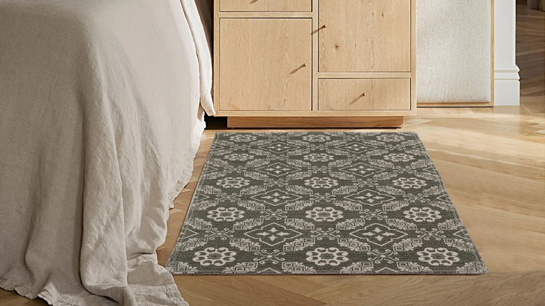 A gray-green patterned accent rug sits next to a bed and a nightstand