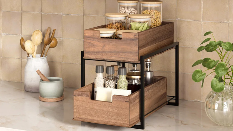 An acacia two-tier organizer with sliding drawers filled with spices and seasonings on a marble countertop