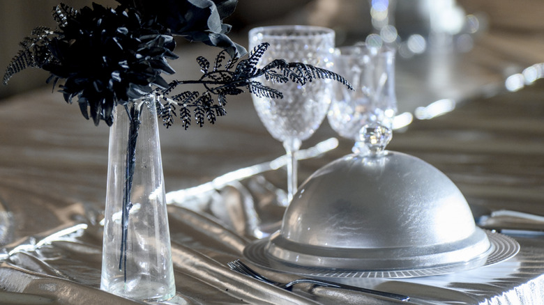 A silver cloche covered a plate sitting on a shimmering silver tablecloth