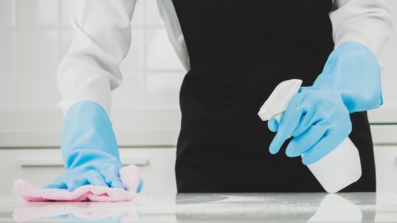 Person cleaning kitchen countertop with vinegar in a spray bottle