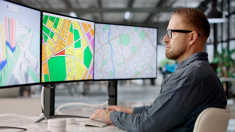 A city planner analyzes maps on three computer monitors.