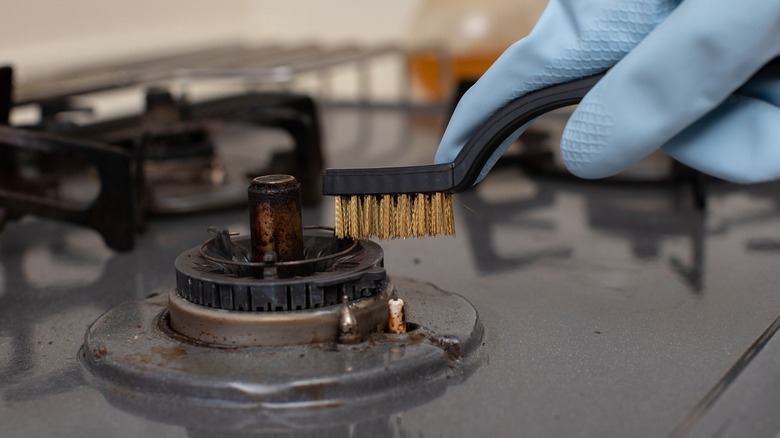 Person wearing rubber gloves cleaning stove burner with a wire brush