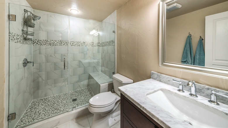 Inside a bathroom with beige walls, gray tiling, and frameless shower glass
