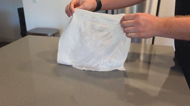 Man using white embossed pattern paper towel to clean wet mess on kitchen countertop