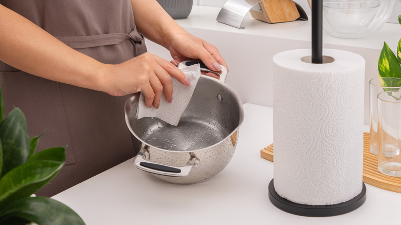 Woman in brown apron using patterned paper towel roll to dry kitchen pan in clean kitchen