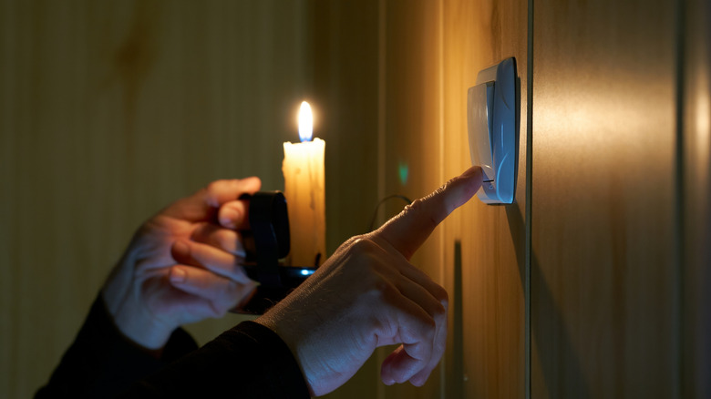 A hand holding a lit candle and pressing a switch with the other