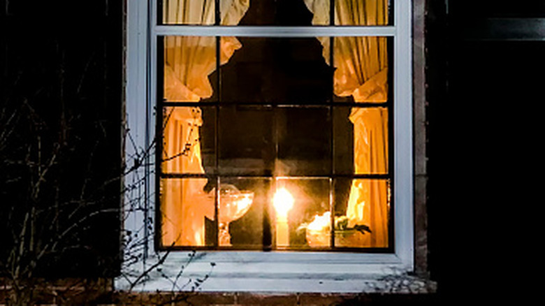 A lone burning candle in the window of a house