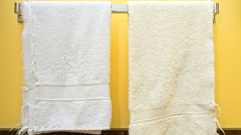 A new white hand towel hanging next to an old yellowing one on a towel rack