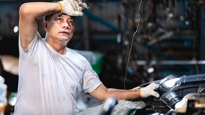 man in white tee shirt sweating over car in garage