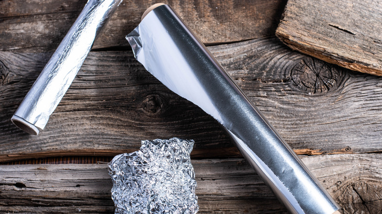 Two rolls of aluminum foil and a ball of foil against wood boards.