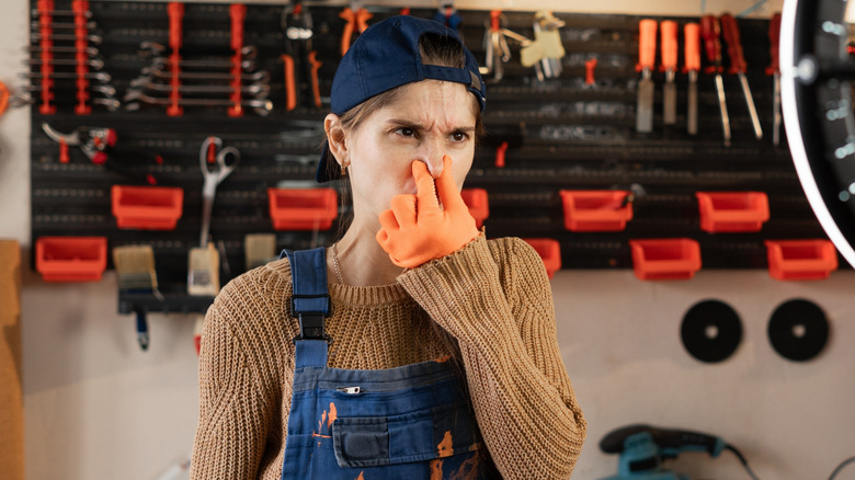 Woman in garage pinching her nose at smelly tools
