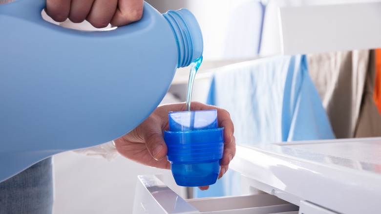 Person measuring liquid laundry detergent in a lid
