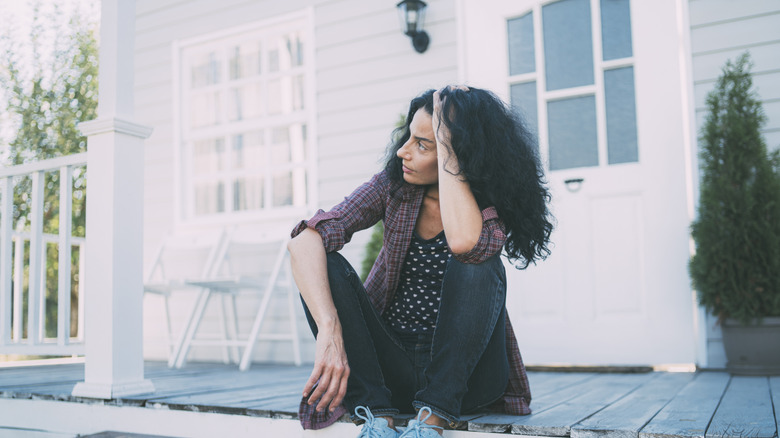A woman looks annoyed as she sits on her porch with a light behind her