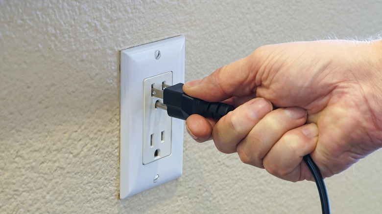 A hand plugging a plug into a three-pronged outlet
