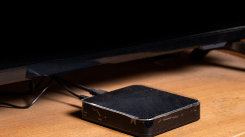 A typcial small black media streaming box in front of a television