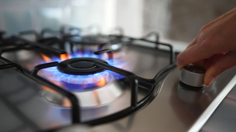 A person turns on a gas stove and the flames are blue and orange