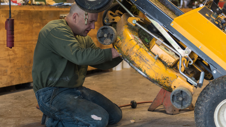 A man inspecting the underside of a yellow riding lawnmower.